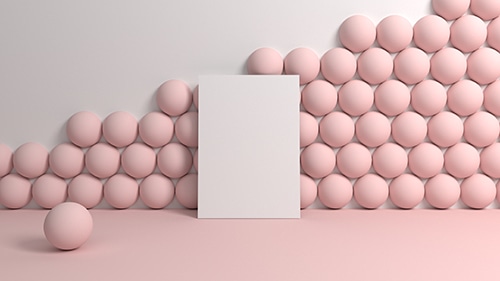 A piece of card leaning against a wall in a room with pink floors, a white wall, and pink balls stacked against the wall