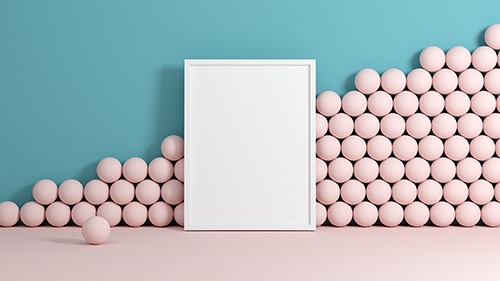 An empty white picture frame leaning against a wall in a room with pink floors, a blue wall, and pink balls stacked against the wall