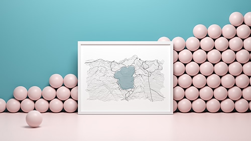 A map in a white picture frame leaning against a wall in a room with pink floors, a blue wall, and pink balls stacked against the wall