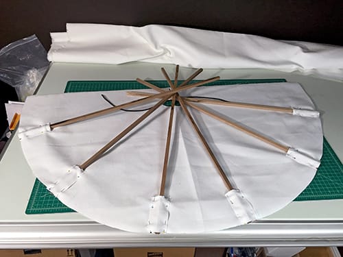 Six wooden poles being sewn into the white tipi fabric