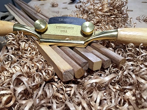 Wooden poles lying on a bed of wood shavings, with a woodworking tool sitting atop them