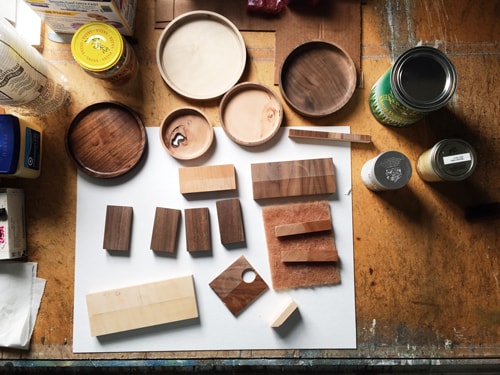 Cans and jars and pieces of wood lying on a table with different finishes applied to them